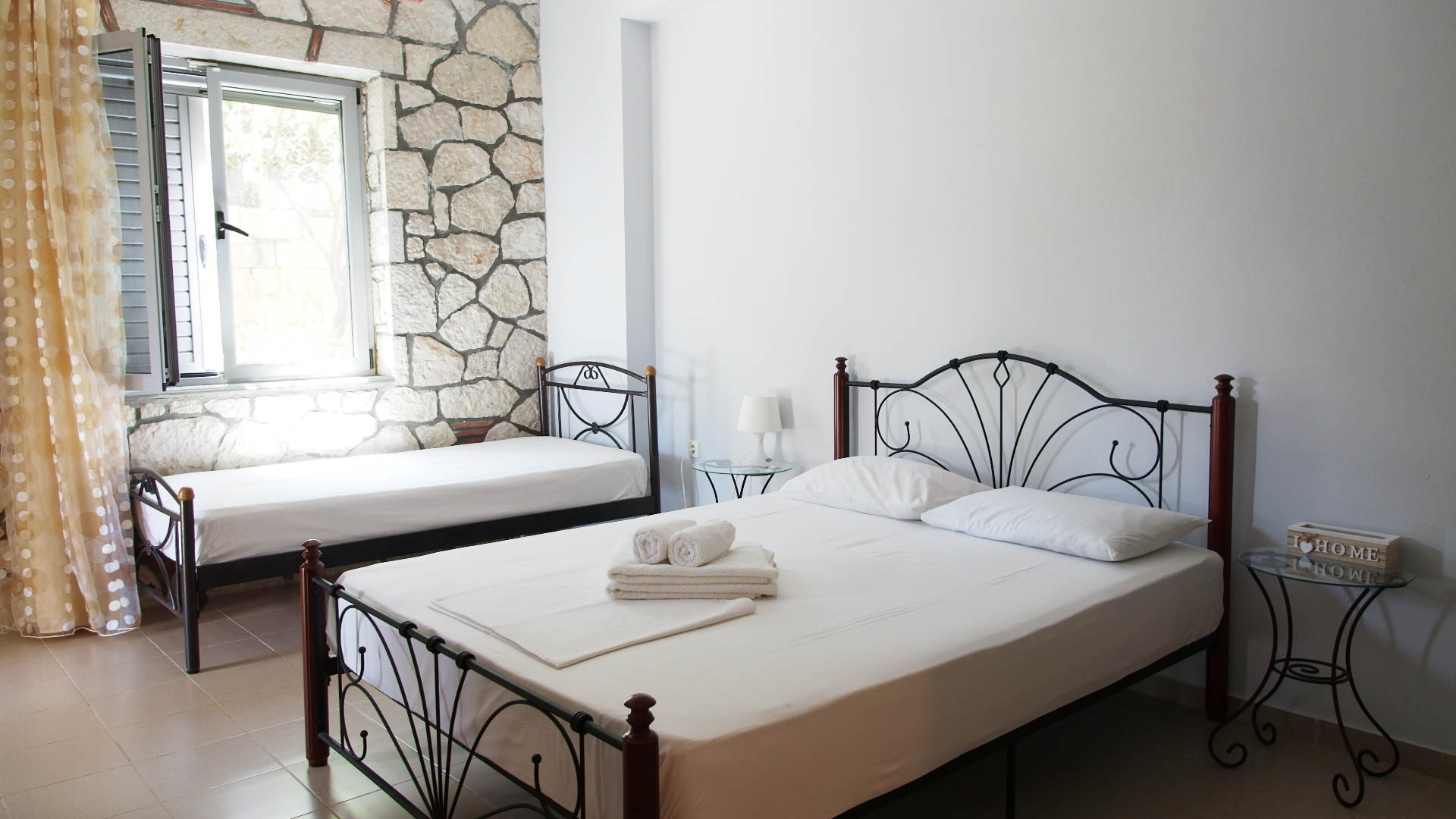 A single bed and double bed next to the window and a stone wall behind.